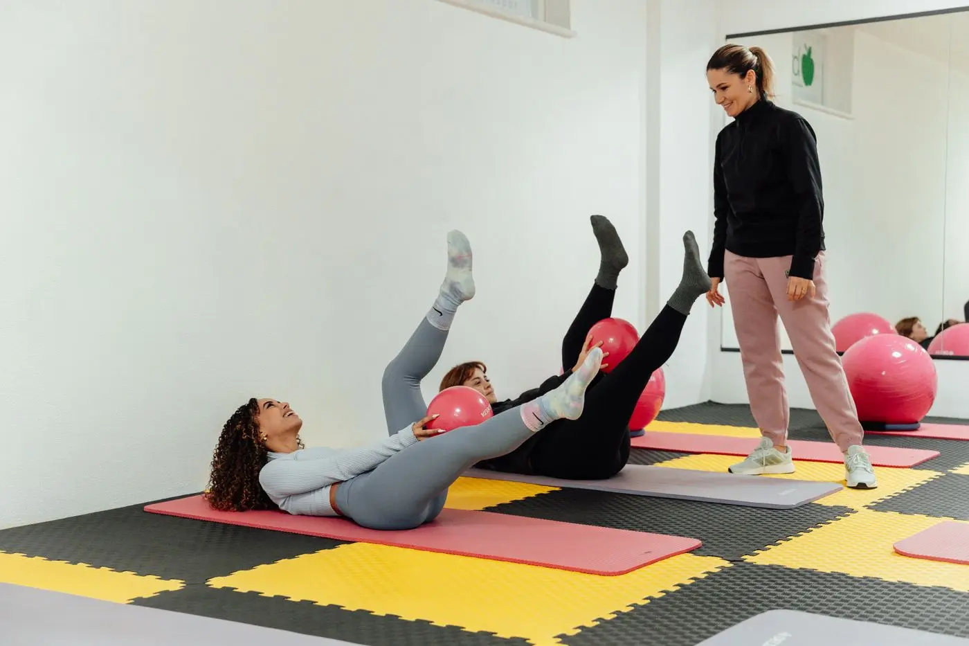 Adultes pratiquant un exercice de Pilates au sol avec de petits ballons sous la conduite d’une intervenante
